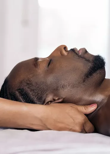 A massage therapist works on a Black man's head and neck area.