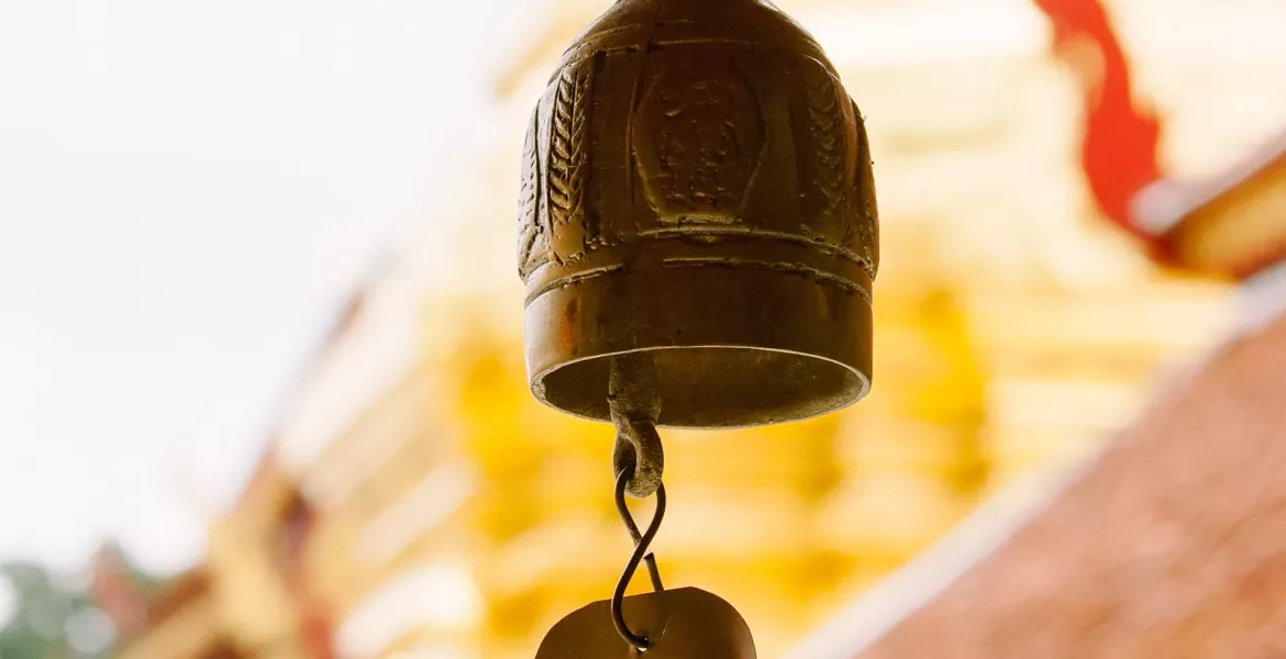 a metal bell hangs outside a gold and yellow wat temple in Thailand.